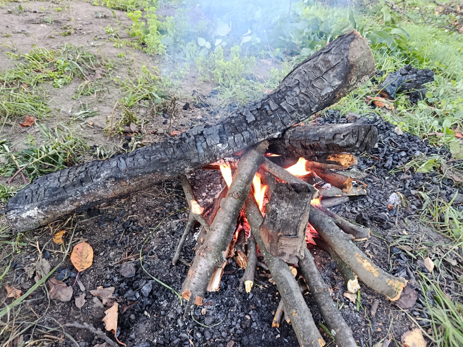 Dwa grube, nadpalone polana położone w poprzek nad płonącym ogniskiem tipi, pod nimi żar i płomienie