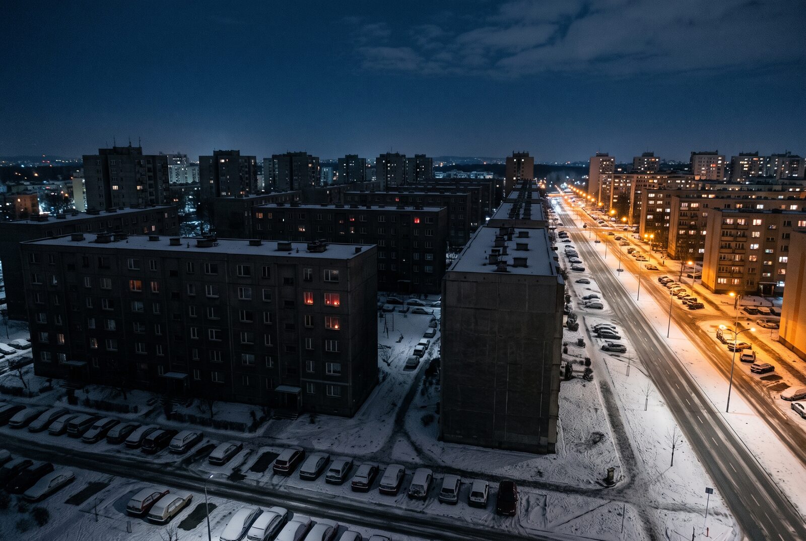 Blackout in a city at night: a block of flats estate without power, next to a district with street lights and lit windows