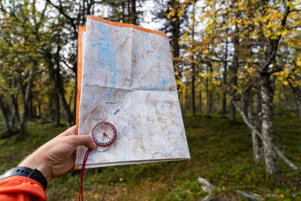 A topographic map and a baseplate compass held in one hand in an autumn forest, getting ready to walk on a compass bearing