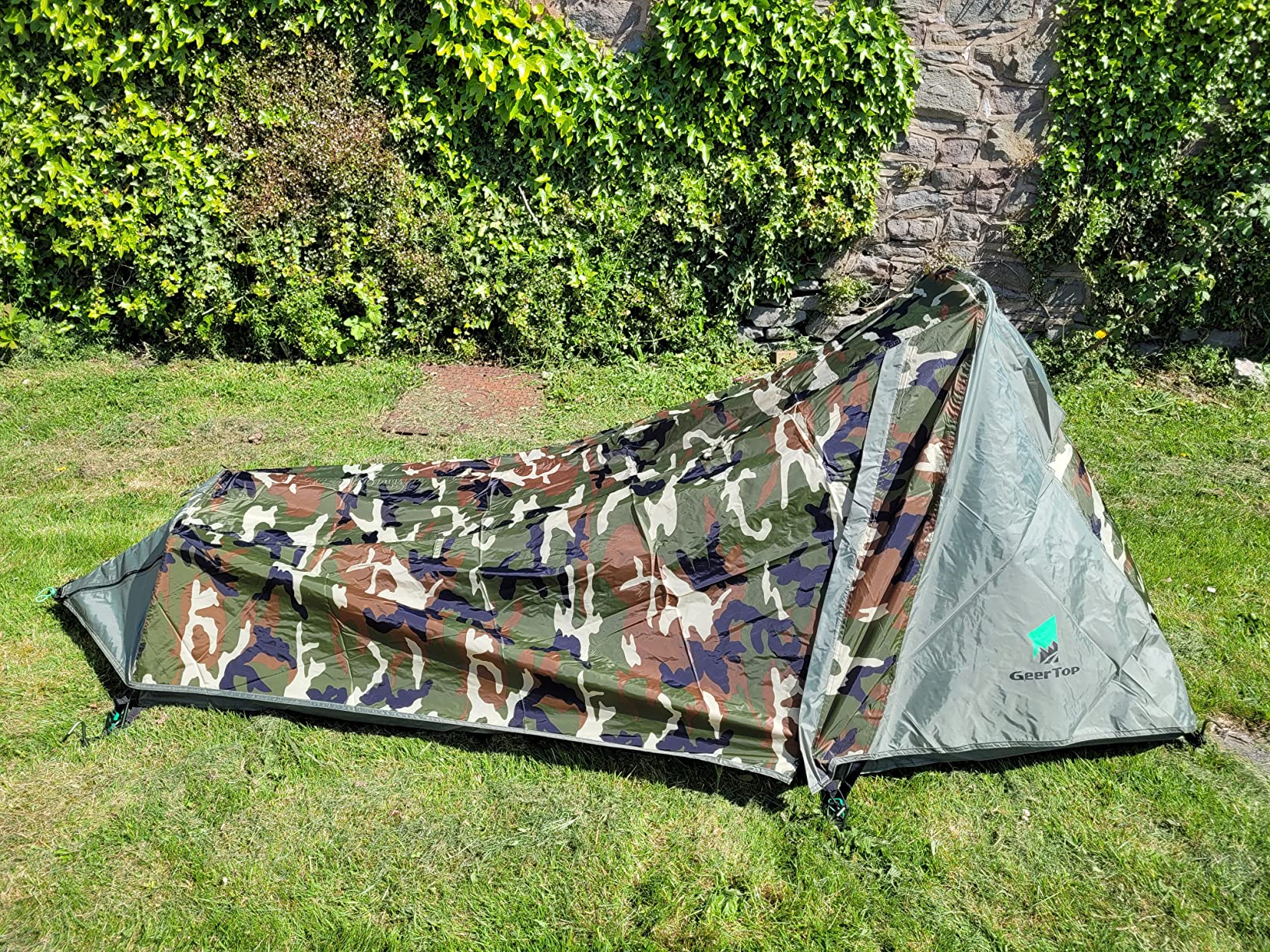 Camo Geertop bivy tent pitched in a garden by an ivy-covered wall