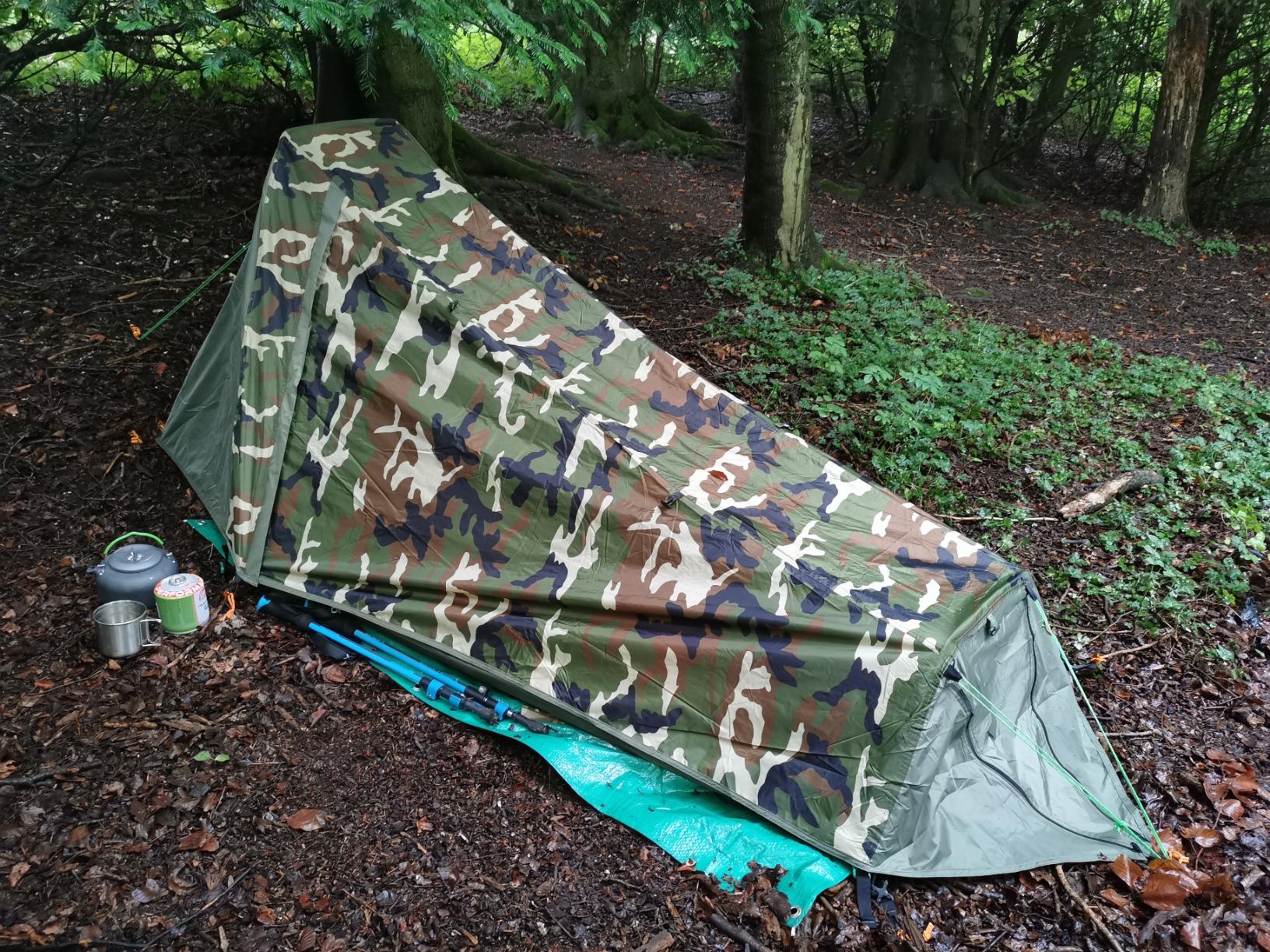 Geertop tent in a forest on a blue groundsheet, a pot and a mug beside it