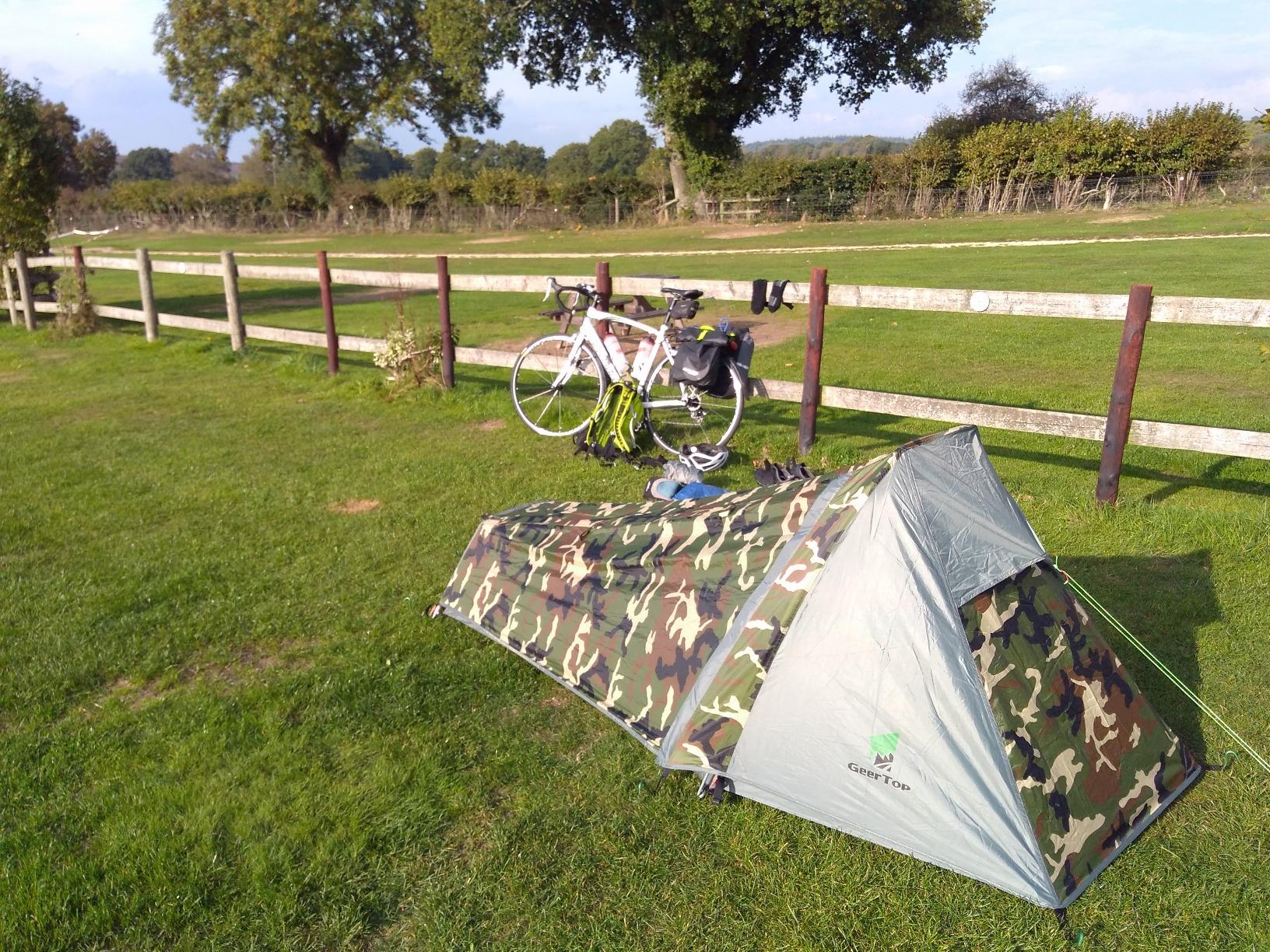 Low one-person Geertop tent in a meadow, a bike leaning on a fence nearby