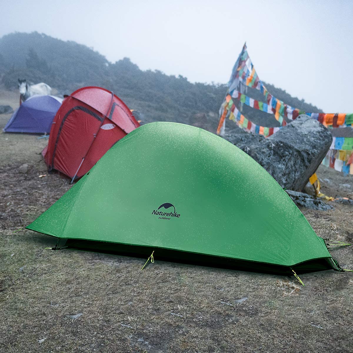 Green Naturehike Cloud-Up 1 tent on rocky ground, prayer flags and red tents nearby